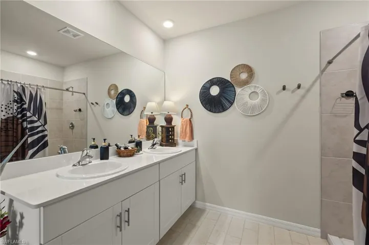Bathroom with visible vents, duel sink, double vanity, and tiled shower