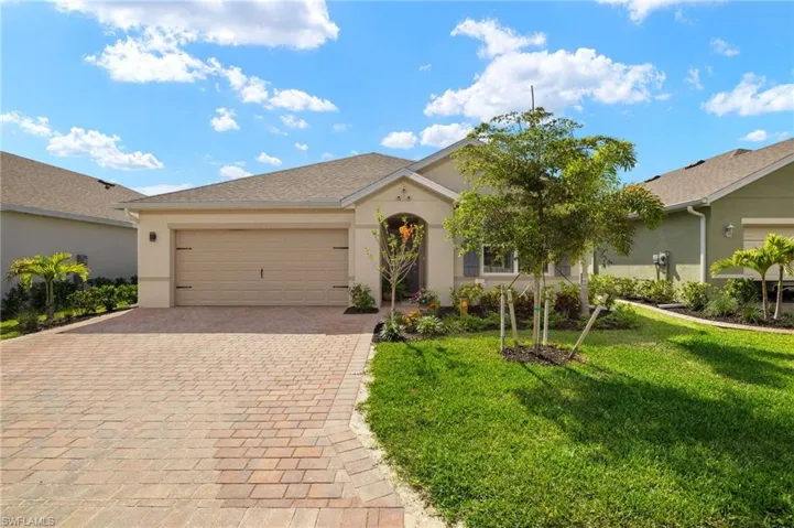 View of front facade with front lawn, driveway, stucco siding, and a garage