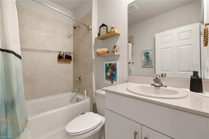 Full bath featuring visible vents, shower / bathtub combination with curtain, toilet, and vanity