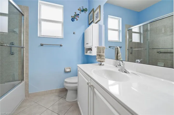 Full bath with light tile patterned flooring, vanity, and combined bath / shower with glass door