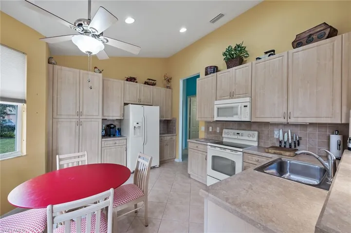 Kitchen featuring decorative backsplash, white appliances, light tile patterned floors, light countertops, and light brown cabinetry