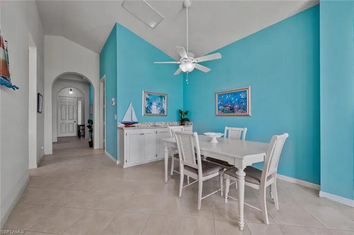Dining area with arched walkways, a ceiling fan, light tile patterned floors, and high vaulted ceiling