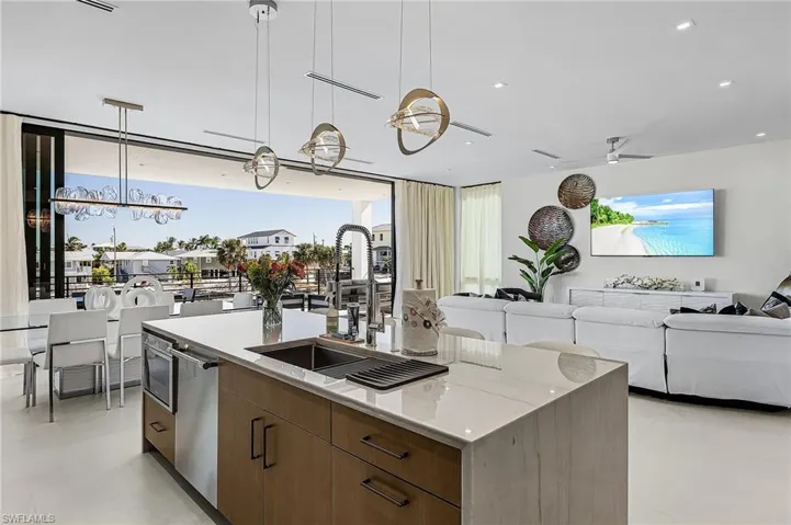 Kitchen featuring brown cabinetry, hanging light fixtures, modern cabinets, open floor plan, and a kitchen island with sink - Virtually Edited Image
