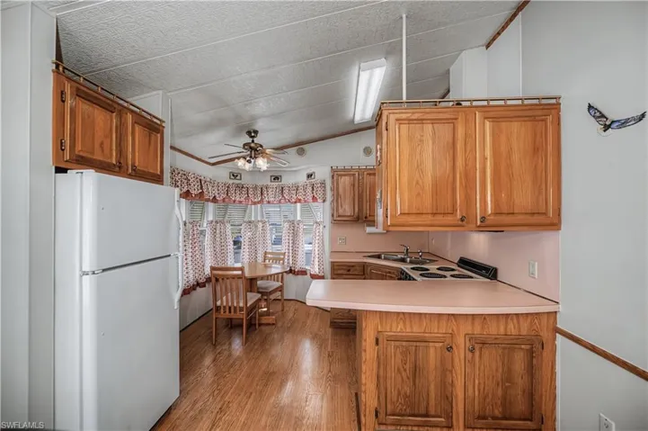Kitchen featuring light countertops, white appliances, ceiling fan, wood finish cabinetry, and vaulted ceiling