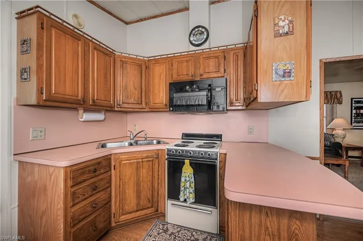 Kitchen with white electric range oven, wood finish cabinetry, black microwave, and light countertops