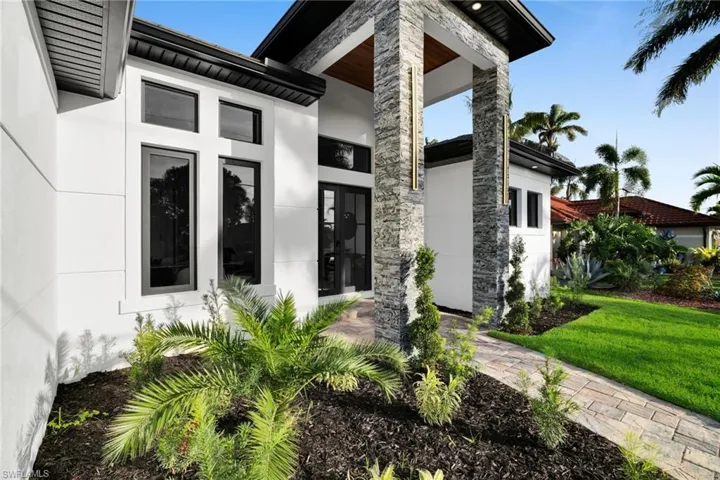 Entrance to property featuring stucco siding, a lawn, and stone siding