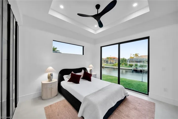 Bedroom featuring a raised ceiling, a water view, multiple windows, and recessed lighting