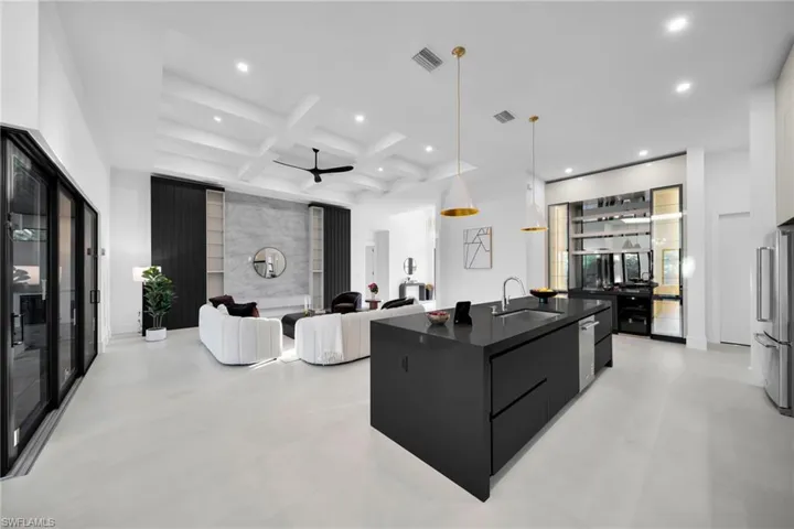 Kitchen with pendant lighting, dark cabinets, an island with sink, coffered ceiling, and beam ceiling