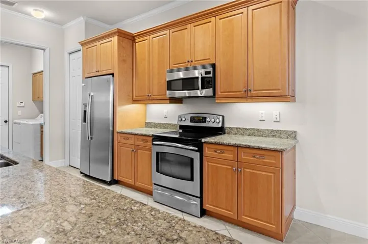 Kitchen with light tile patterned floors, light stone countertops, ornamental molding, appliances with stainless steel finishes, and separate washer and dryer