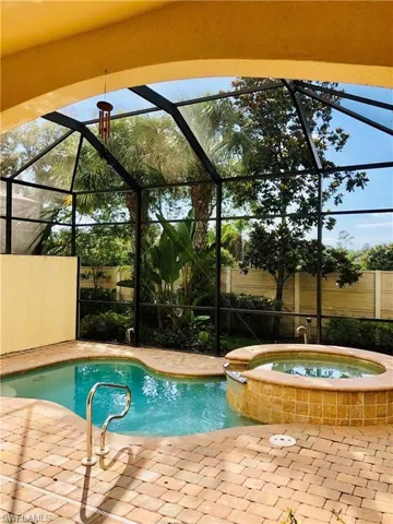 View of swimming pool with an in ground hot tub, glass enclosure, and a patio