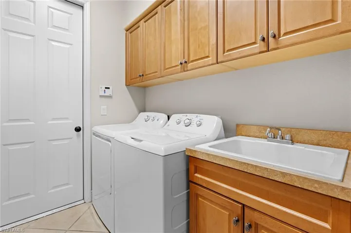 Laundry room featuring cabinets, light tile patterned floors, washing machine and dryer, and sink