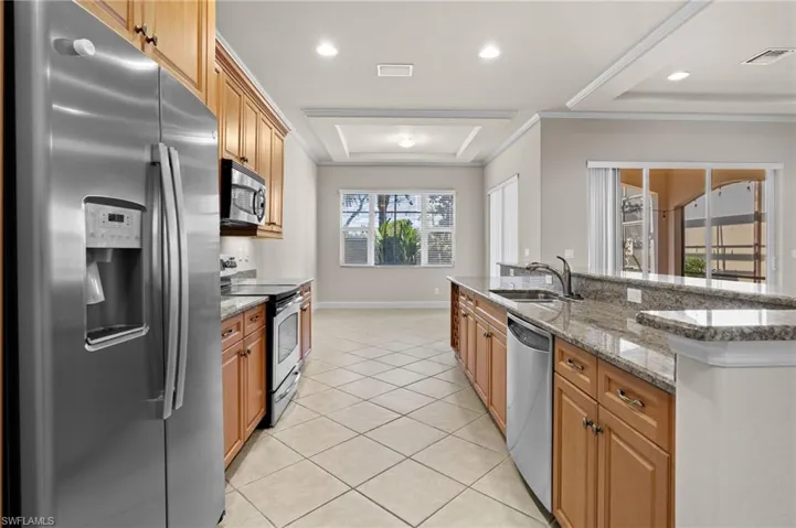 Kitchen with a center island with sink, sink, light tile patterned floors, light stone countertops, and appliances with stainless steel finishes