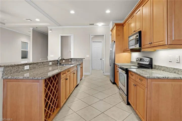 Kitchen with stainless steel appliances, light stone counters, crown molding, and sink