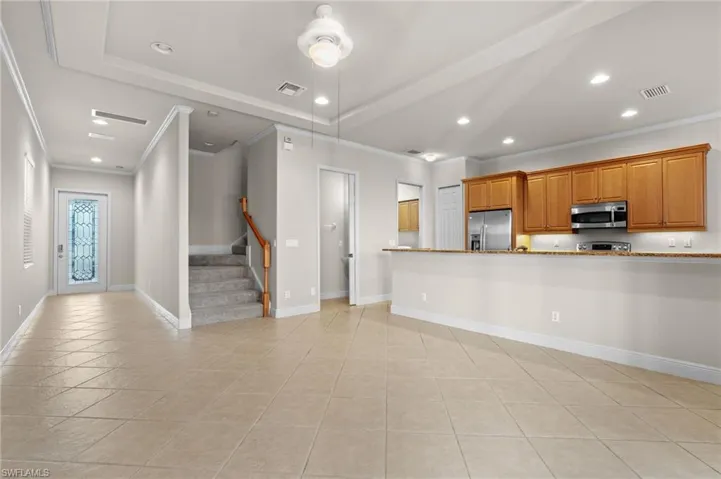 Kitchen with light stone counters, light tile patterned floors, ornamental molding, and appliances with stainless steel finishes