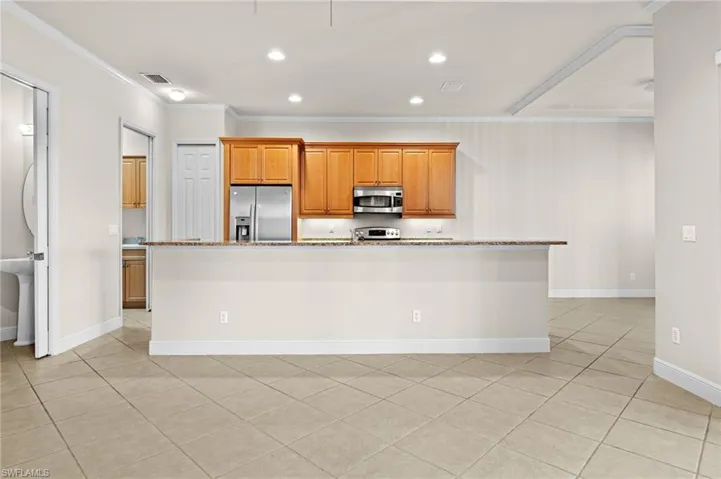 Kitchen with light stone countertops, stainless steel appliances, crown molding, a center island with sink, and light tile patterned flooring