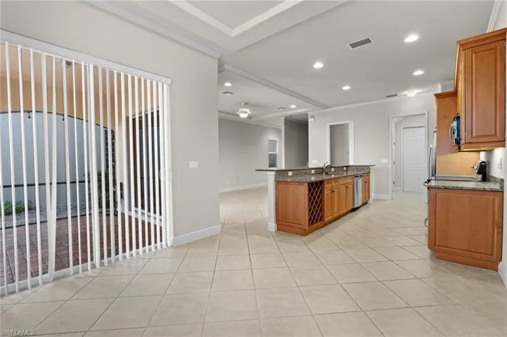 Kitchen featuring stone counters, stainless steel appliances, an island with sink, light tile patterned floors, and ornamental molding