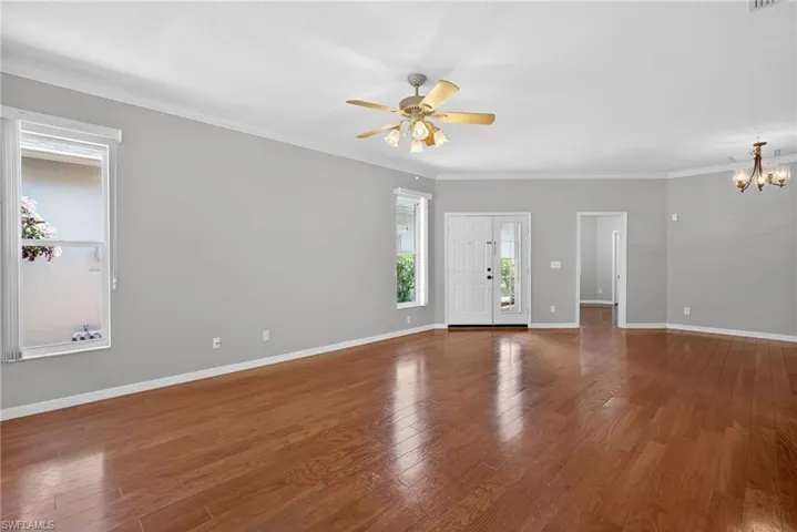 Unfurnished living room featuring dark wood finished floors, a ceiling fan, crown molding, and a chandelier