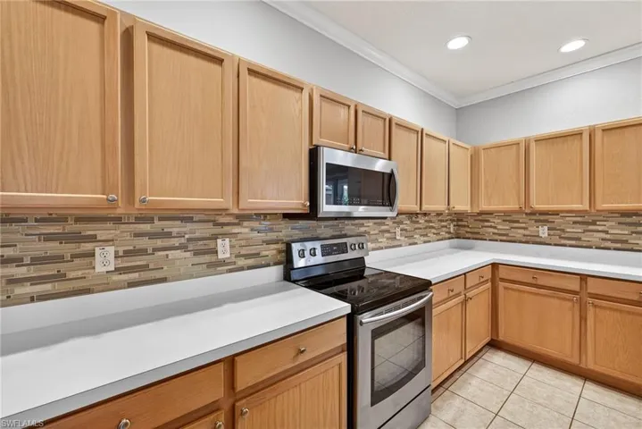 Kitchen with stainless steel appliances, light countertops, crown molding, light tile patterned floors, and decorative backsplash