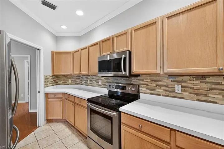 Kitchen featuring stainless steel appliances, light tile patterned floors, light countertops, crown molding, and light wood finish cabinetry
