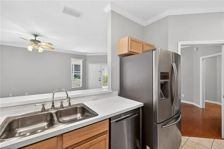 Kitchen featuring ornamental molding, stainless steel appliances, light countertops, ceiling fan, and light wood finish cabinetry