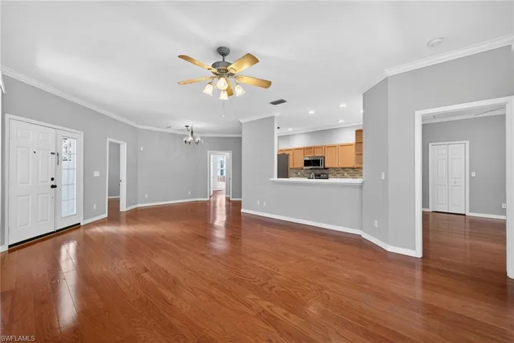 Unfurnished living room featuring dark wood finished floors, crown molding, a ceiling fan, and suspended lighting