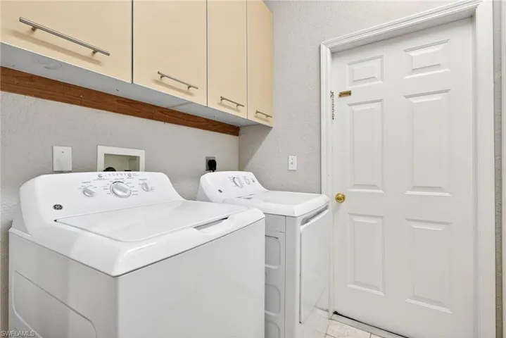 Laundry area featuring a textured wall, independent washer and dryer, and cabinet space