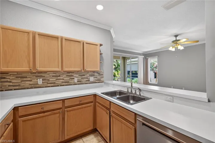 Kitchen with crown molding, light countertops, backsplash, a ceiling fan, and stainless steel dishwasher