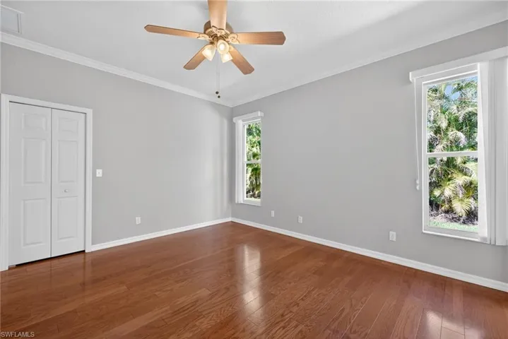 Unfurnished bedroom with ornamental molding, dark wood-type flooring, ceiling fan, and a closet