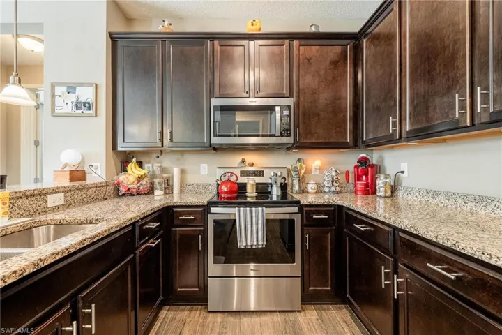 Kitchen with decorative light fixtures, appliances with stainless steel finishes, light stone counters, and light hardwood / wood-style floors