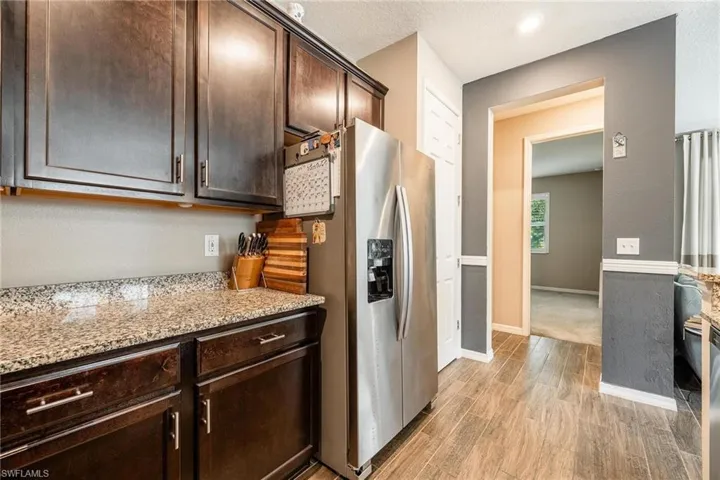 Kitchen with light wood-type flooring, stainless steel fridge, dark brown cabinets, and light stone counters