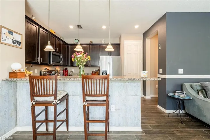 Kitchen with appliances with stainless steel finishes, dark brown cabinets, a breakfast bar area, and light stone countertops