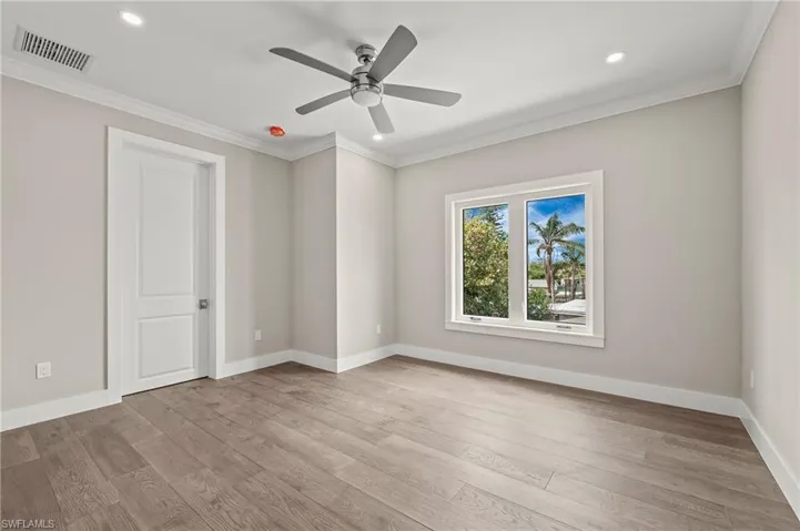 Spare room featuring wood finished floors, baseboards, visible vents, ceiling fan, and ornamental molding