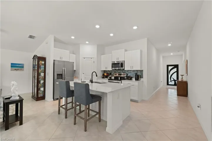 Kitchen featuring stainless steel appliances, a breakfast bar area, backsplash, light tile patterned flooring, and a center island with sink
