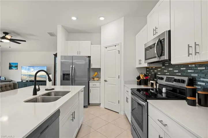Kitchen featuring appliances with stainless steel finishes, light countertops, decorative backsplash, a ceiling fan, and white cabinets