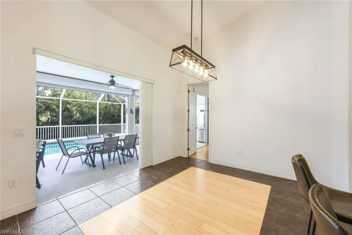 Dining area with dark tile floors with wood-look inlay, high vaulted ceiling, and light fixture