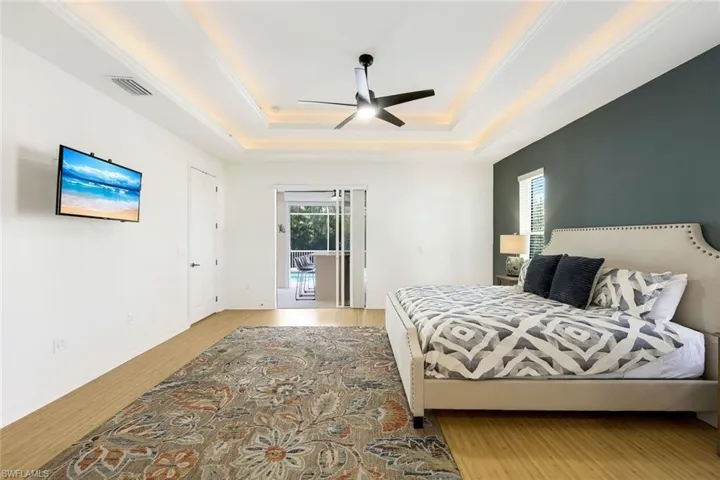 Bedroom with tray ceiling, ornamental molding, light wood-type flooring, and ceiling fan