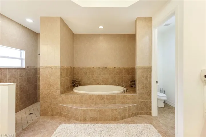 Bathroom with toilet, independent shower and bath, tile patterned floors, and tile walls