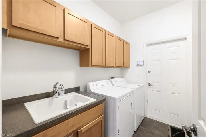 Washroom with dark tile patterned floors, sink, separate washer and dryer, and cabinets