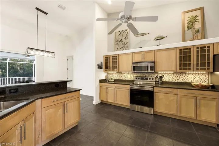 Kitchen with light brown cabinets, backsplash, a high ceiling, pendant lighting, and stainless steel appliances