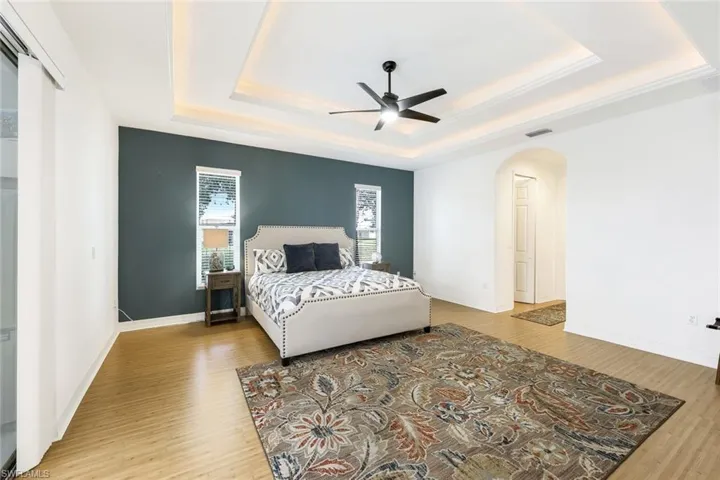 Bedroom featuring ceiling fan, a raised ceiling, and wood-look flooring