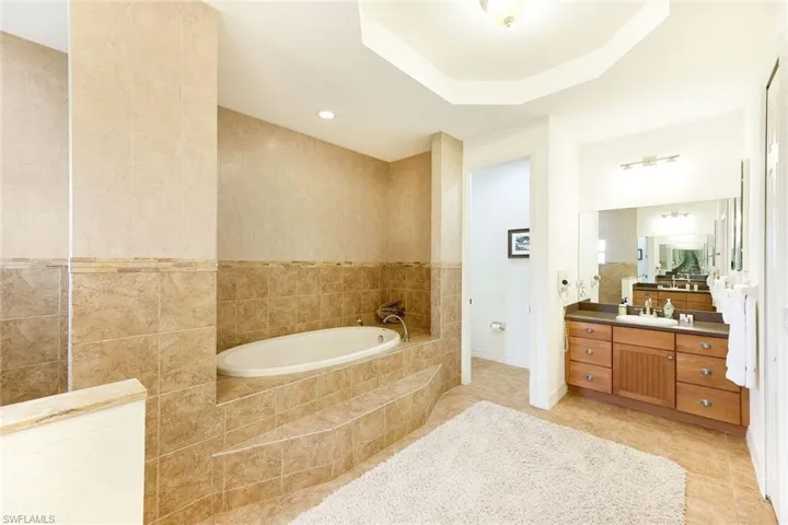 Bathroom with vanity, a relaxing tiled tub, a tray ceiling, and tile walls