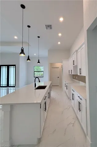 Kitchen with white cabinets, a kitchen island with sink, decorative light fixtures, recessed lighting, and light marble finish flooring