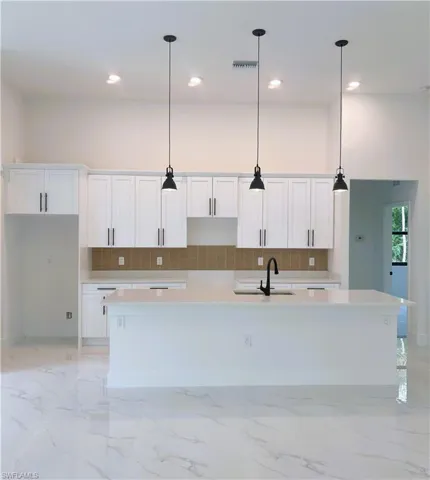 Kitchen featuring decorative backsplash, white cabinets, light stone counters, and recessed lighting