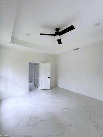 Unfurnished bedroom with a tray ceiling, a ceiling fan, and light marble finish flooring