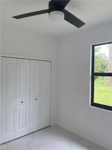 Unfurnished bedroom featuring marble look tiles, a ceiling fan, and a closet