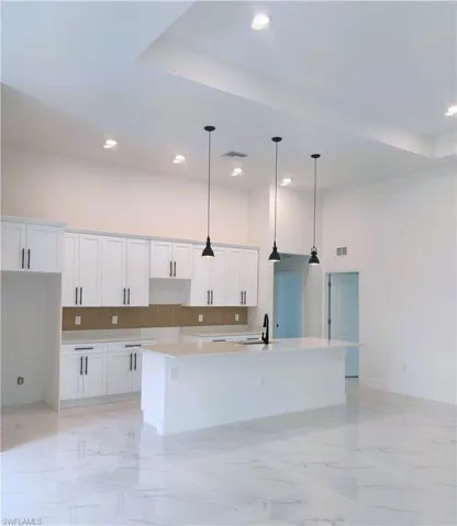 Kitchen with tasteful backsplash, white cabinetry, light marble finish floors, a high ceiling, and recessed lighting