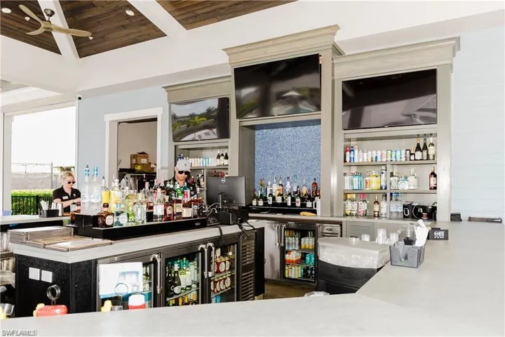 Indoor wet bar featuring light countertops, ceiling fan, and a wood ceiling with exposed beams
