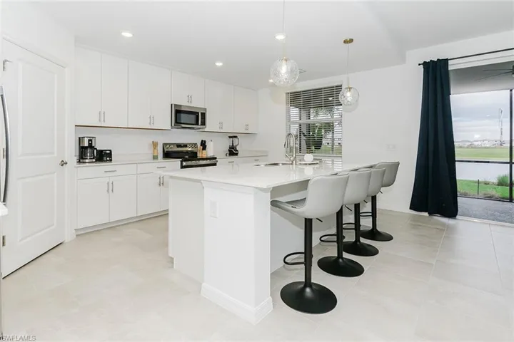 Kitchen with stainless steel appliances, pendant lighting, white cabinets, a center island with sink, and a breakfast bar area