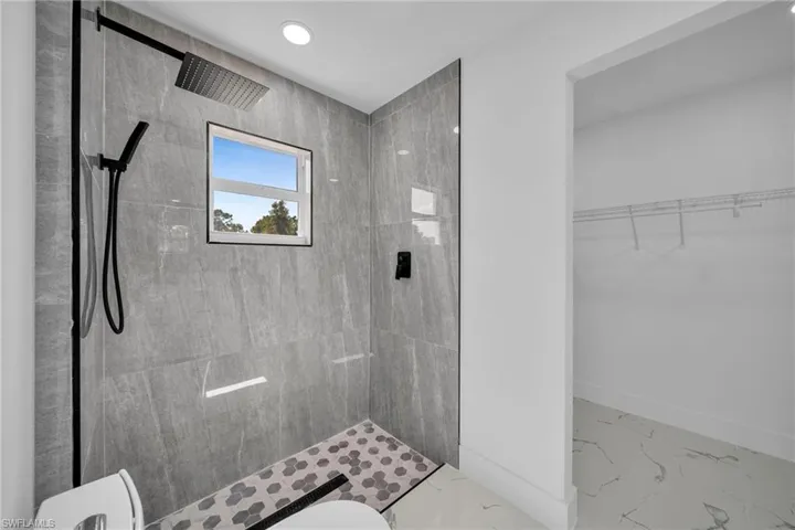Bathroom featuring a walk in closet, a stall shower, marble look tiles, and recessed lighting