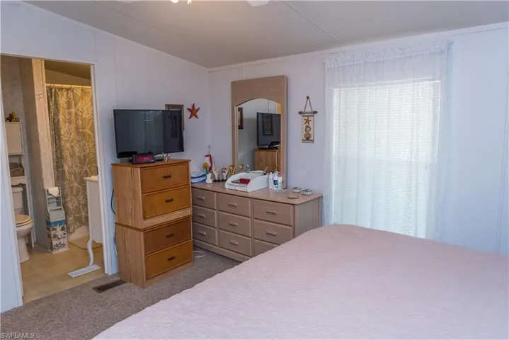 Bedroom with vaulted ceiling, ensuite bath, a ceiling fan, and light colored carpet